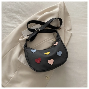 Detail of black crescent hobo bag featuring colorful leather heart patches and gold zipper