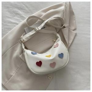 Detail of white crescent bag showing colorful heart patches and smooth faux leather texture