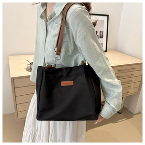 Detail of black nylon tote bag with brown leather straps and silver metal hardware