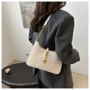 Détail du sac baguette en cuir ivoire avec chaîne dorée sur une veste blazer