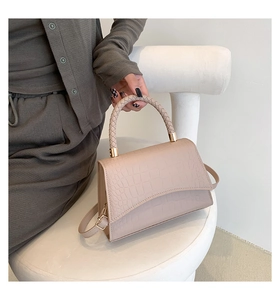 Detail of crocodile pattern beige bag with woven handle and gold-tone hardware on white stand