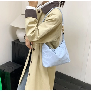 Detail of light blue hobo bag with pleated texture and beaded charm on beige coat