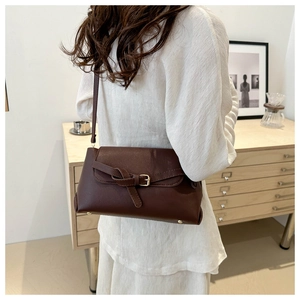 Detail of dark brown leather crossbody bag with buckle and knot strap on a model