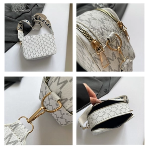 Detail view of white camera bag with M-pattern, wide strap, and dual gold zippers