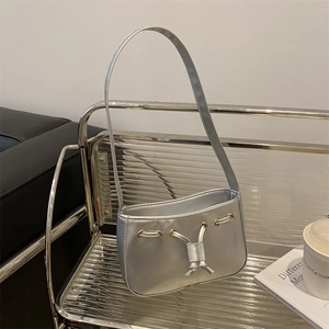 Minimalist silver shoulder bag with metallic finish and drawstring detail on a shelf