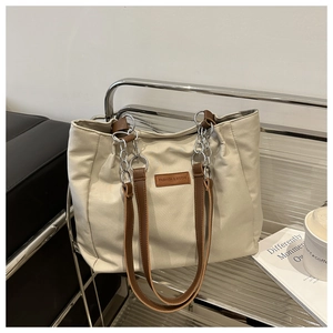 Detail of canvas tote bag with brown leather strap and silver chain on a metal stand