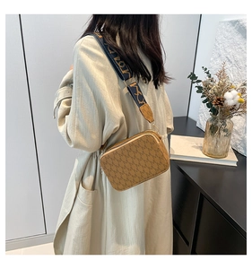 Brown crossbody bag with 'M' monogram and colorful wide woven strap shown on beige coat