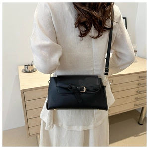 Detail of a minimalist black leather crossbody bag with gold hardware on a model