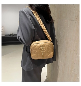 Détail du sac bandoulière matelassé kaki avec boucle lettre dorée et pompon sur l'épaule