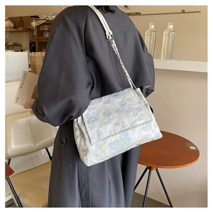 Detail of white cloth shoulder bag with blue butterfly embroidery on a cafe table
