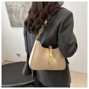 Détail d'un sac hobo beige chic avec chaîne dorée porté sur un blazer noir élégant