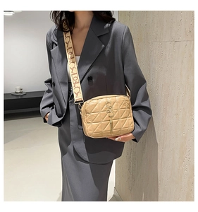 Détail du sac beige matelassé avec logo en métal, pompon et bandoulière imprimée