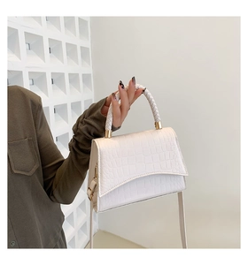 Detail of white crocodile pattern square bag featuring a woven round top handle and gold hardware