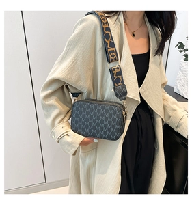 Close-up of stylish crossbody bag featuring letter patterns and a wide woven shoulder strap