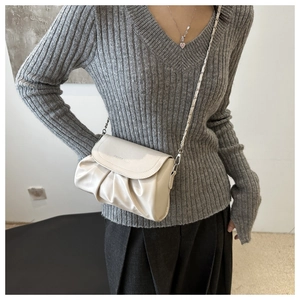 Gros plan d'un sac plissé crème avec bandoulière chaîne porté par un mannequin