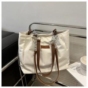 Detail of white canvas tote bag with brown leather handles and decorative silver chain links