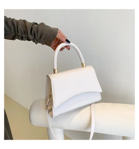 Close-up of white crocodile pattern flap bag with braided handle and gold hardware