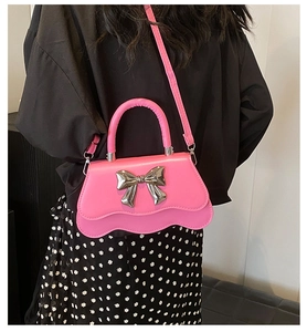 Détail d'un sac à main rose avec un grand nœud métallique argenté et bord ondulé