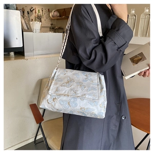 Detail of white butterfly embroidery shoulder bag with metal chain on a model