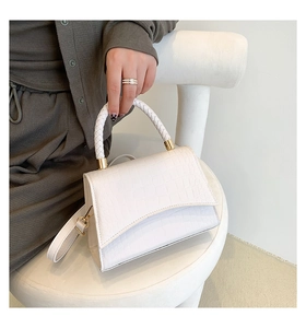 Detail of white crocodile pattern handbag with woven handle and gold hardware on a chair