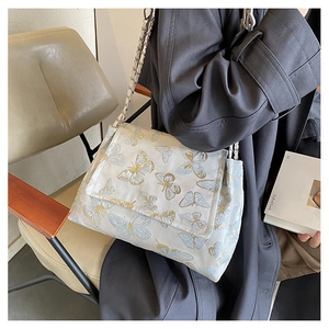 Détail d'un sac à bandoulière crème avec broderies papillon et bandoulière en chaîne