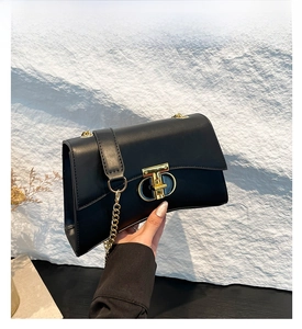 Détail du sac noir avec bandoulière en chaîne dorée et boucle géométrique en métal