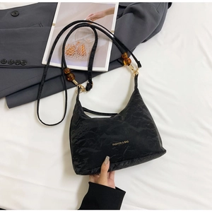 Detail of black tote bag featuring amber beads and golden chain with soft pleated texture