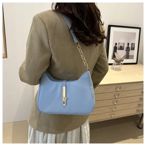 Sky blue leather underarm bag with gold chain strap and metal lock shown on a shoulder