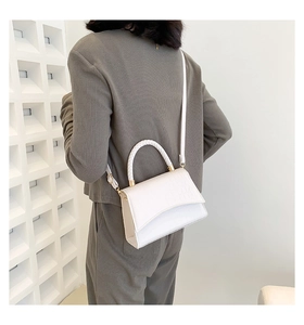 Detail view of white crocodile pattern square bag with woven handle worn by model