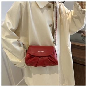 Détail du sac bandoulière rouge plissé avec chaîne argentée sur un manteau crème