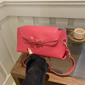 Rose pink faux leather crossbody bag with golden buckle and adjustable strap held by hand