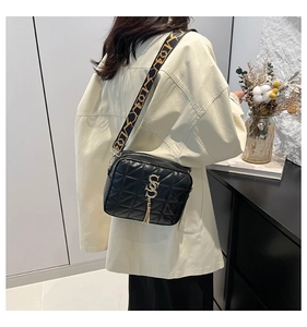 Détail du sac bandoulière matelassé noir avec fermoir doré en S, pompon et sangle imprimée