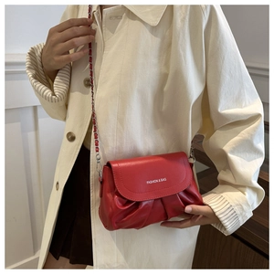 Détail d'un sac à bandoulière rouge plissé avec chaîne en métal porté par un mannequin