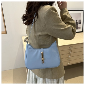 Detail of light blue crescent bag with golden clasp worn over a khaki blazer