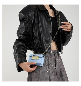 Close-up of light blue mini square bag with gold chain strap on dark leather jacket