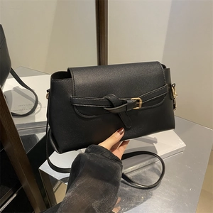 Black leather crossbody bag with flap and gold metal buckle on modern display
