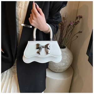 Détail du sac à main blanc à bords ondulés avec nœud argenté et poignée anneau