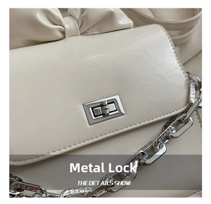 Detail showing creamy leather surface with silver twist lock and bow decoration on the bag