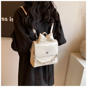Detail of cream white leather backpack featuring 3D bow and silver metal chain detail