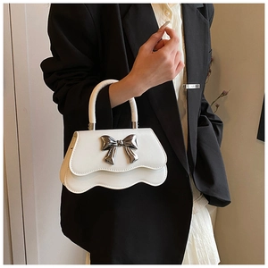 Détail du sac à main blanc à bord ondulé avec un grand nœud argenté et cuir lisse