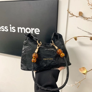 Minimalist black pleated tote bag with orange bead handle detail and gold hardware