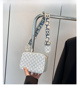 Close-up of white crossbody bag with M-pattern print and wide fabric shoulder strap