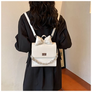 Detail view of cream white mini backpack with large bow and silver chain on model