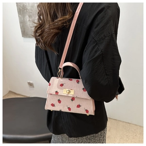 Detail of pink corduroy mini bag featuring red strawberry print and golden metal twist lock