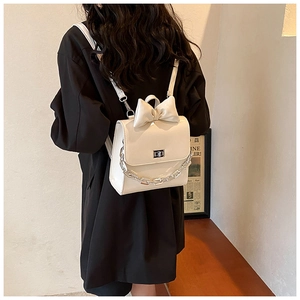 Rear view of a cream mini backpack with a large bow and decorative silver chain