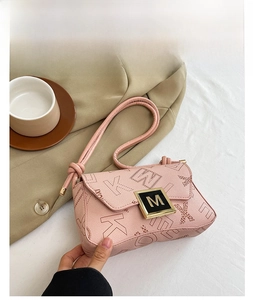 Close-up detail of pink leather shoulder bag with embossed letters and M-shaped metal buckle