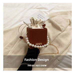 Detail of a brown bucket bag with a pearl handle and drawstring closure on fabric