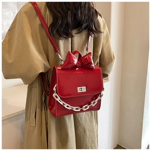 Rear view of a shiny red patent leather backpack with a bow and silver chain on a model