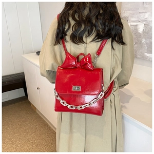 Detail of red patent leather backpack with large bow, silver chain and turn-lock closure