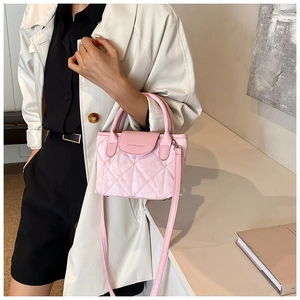 Close-up of pink quilted bucket bag with chain strap held by model in casual outfit